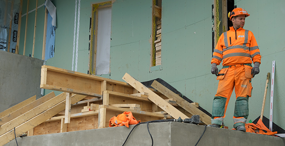 Mann i oransje arbeidsklær står på toppen av murtrapp under konstruksjon
